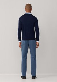 Marine gebreide trui, lichtblauw collared shirt eronder, gecombineerd met lichtblauwe broek en zwarte schoenen. Klassieke pasvorm en gladde textuur.