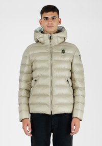 Beige pufferjakke med hætte, lynlås foran, elastiske cuffs og to sidelommer; let, skinnende materiale med quiltet design.
