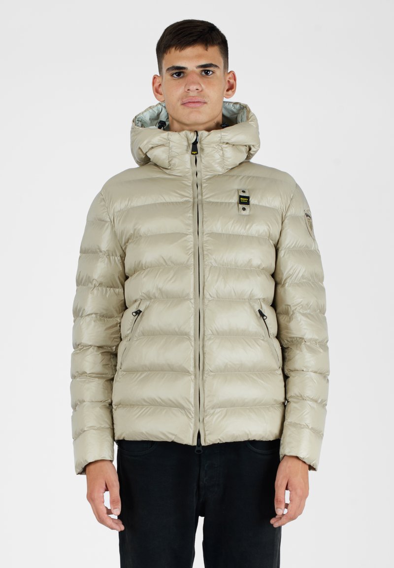Beige pufferjakke med hætte, lynlås foran, elastiske cuffs og to sidelommer; let, skinnende materiale med quiltet design.