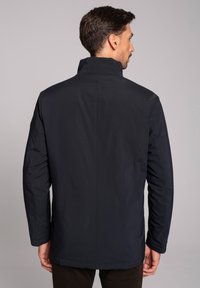 Męska ciemnoniebieska wodoodporna kurtka, z wysokim kołnierzem, długimi rękawami oraz gładką, matową fakturą z minimalnymi detalami przeszyć.