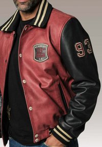 Veste varsity en cuir rouge avec des manches en cuir noir, col côtelé rayé, patch brodé avec "18ème campus sud" et le numéro "93". Fermetures à boutons.