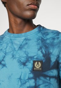 Blue tie-dye sweatshirt featuring a round neckline, textured fabric, and a patch with the brand logo on the front.