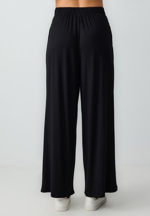 Pantalons larges noirs en tissu doux et extensible ; dotés d'une taille élastique et de poches latérales pour plus de praticité.