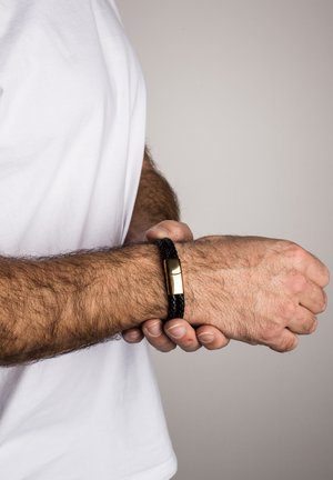 Black braided leather bracelet with a gold-toned metal clasp. The design is flexible and wraps around the wrist.