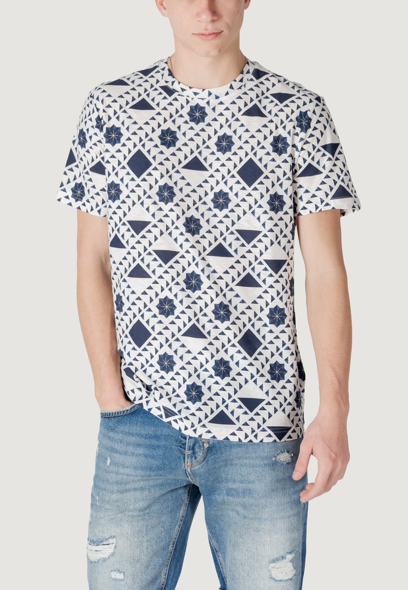 T-shirt navy e bianco con motivi geometrici, maniche corte, scollatura rotonda e vestibilità casual. Indossato con jeans chiari strappati.