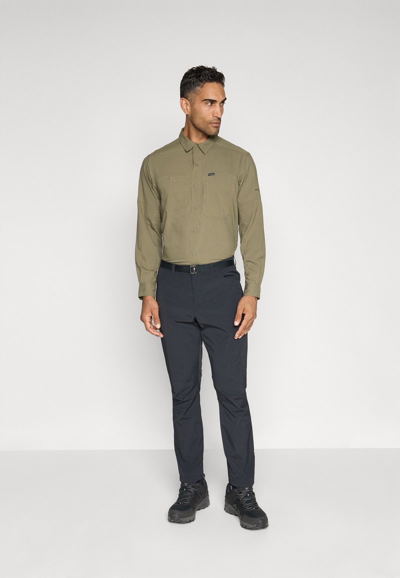 Khakifarbenes Langarmhemd mit Button-Down-Kragen und zwei Brusttaschen, kombiniert mit dunklen Hosen und schwarzen Schuhen. Einfaches, funktionales Design.