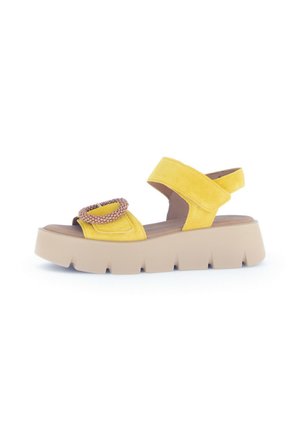 Yellow suede sandal with a wide strap, decorative circular accent, and a chunky beige platform sole. Open-back design for easy wear.