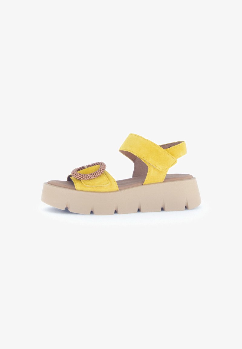Yellow suede sandal with a wide strap, decorative circular accent, and a chunky beige platform sole. Open-back design for easy wear.