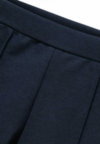 Granatowy materiał o gładkiej strukturze z detalami plisa i elastycznym pasem. Prosty, czysty design bez widocznych elementów metalowych.