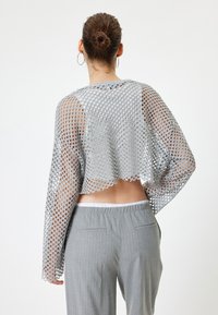 Grijs gebreid cropped top met open mesh ontwerp, lange mouwen en gegolfde zoom, gecombineerd met grijze gestreepte broek.