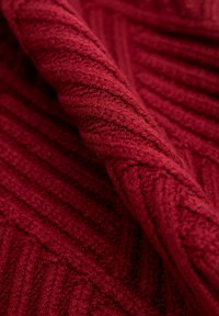 Tissu tricoté rouge avec une texture côtelée, présentant une teinte profonde et une surface douce et duveteuse, mettant en valeur des motifs de points complexes.