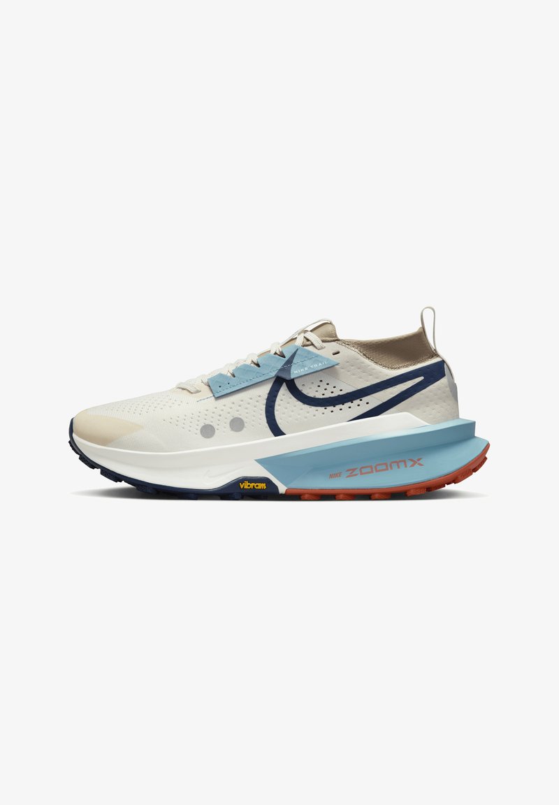 Scarpa da ginnastica bianca e beige chiaro con accenti blu, parte superiore in rete, swoosh navy a contrasto e suola rosso-arancio. Presenta la tecnologia ZoomX.