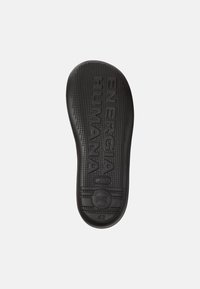 Suole di scarpe in gomma nera con superficie testurizzata, caratterizzate dalla frase in rilievo "ENERGIA HUMANA" e dalla taglia "42". Motivi circolari e lineari.