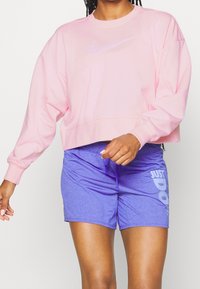 Sweat-shirt court rose avec un swoosh Nike violet clair, associé à un short bleu arborant un logo "JUST DO IT" blanc.
