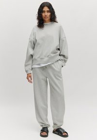 Grijze sweatshirt- en sweatpants-set, gemaakt van zacht materiaal. Kenmerkt zich door een relaxed fit, geribde boorden en een gelaagde look met een witte basis.