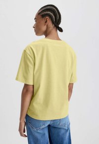 Geel katoenen T-shirt met een relaxte pasvorm, korte mouwen en een ronde hals, gecombineerd met lichtblauwe wijde jeans.