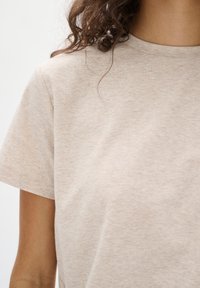 Beige katoenen t-shirt met korte mouwen, een ronde halslijn en een gestructureerde afwerking. De stof heeft een subtiel gemêleerd patroon.
