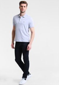 Grå polo med krage, korta ärmar och en liten broderad logotyp. Bärs med mörka jeans och vita sneakers.