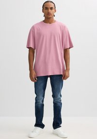 Camiseta de algodón rosa con un corte relajado, mangas cortas, combinada con unos vaqueros azul oscuro y zapatillas blancas. Diseño simple, sin patrones.