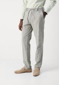 Light gray linen trousers with a relaxed fit, elastic waistband, and drawstring. Paired with beige suede loafers for contrast.