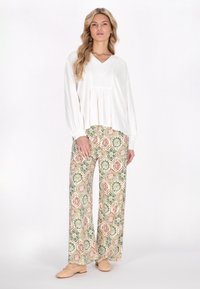 Top bianco a maniche lunghe a scollo a V con dettagli plissettati abbinato a pantaloni larghi con un motivo floreale geometrico colorato in beige, verde e rosso.
