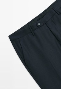 Op maat gemaakte marineblauwe broek van gestructureerde stof, met een enkele knoopsluiting en plooien aan de voorkant.