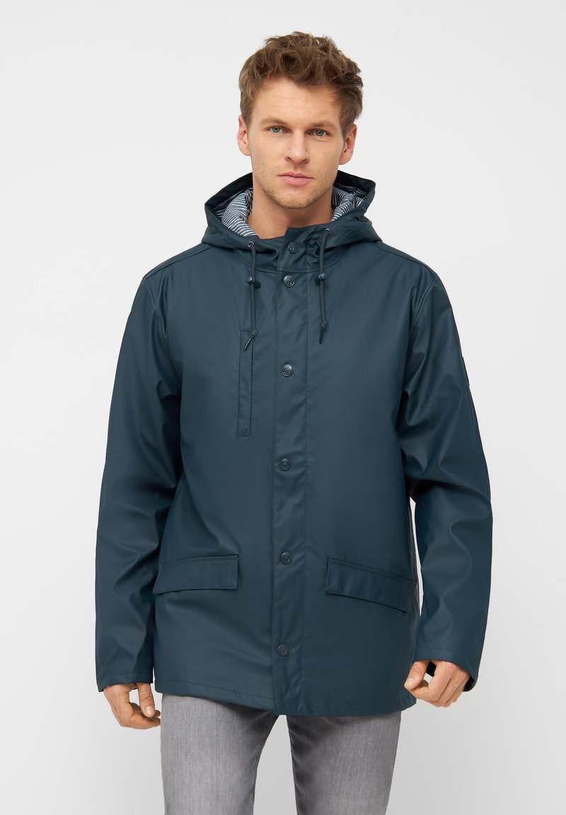 Vandtæt marineblå jakke med hætte, frontlukning med trykknapper, to påsyede lommer og stribet indvendig foer. Blød tekstur og afslappet design.