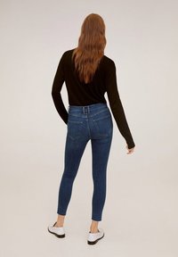 Jeans in denim blu snello con vita alta, due tasche posteriori e orlo frangiato. Abbinati a una maglietta nera a maniche lunghe e scarpe bianche.