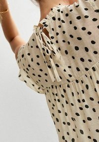 Blusa beige chiaro con pois neri, scollatura arricciata con lacci, vestibilità ampia e tessuto strutturato.