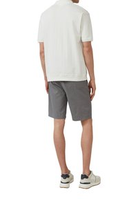 Korte mouwen polo in wit met een verticale ribbelstructuur, gecombineerd met grijze shorts. Schoeisel heeft een mix van witte en marineblauwe accenten.
