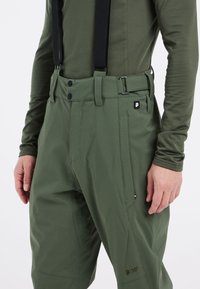 Groene outdoorbroeken met verstelbare zwarte bretels, drukknoopsluitingen, ritszakken en een logo op de onderbeen. Glad, duurzaam materiaal.