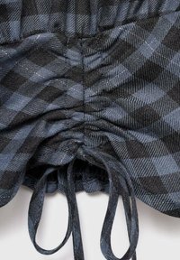 Karirani materijal u nijansama plave i crne s nabranim strukom. Ima vrpce za podešavanje i teksturiranu površinu.