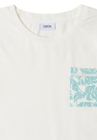 T-shirt blanc à col rond avec une poche poitrine à motif feuilles tropicales bleu sarcelle et blanc et une étiquette de marque CECIL à l'intérieur du col.