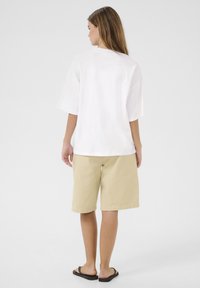 Witte oversized T-shirt, beige knielange shorts, platte zwarte sandalen, gladde katoenen textuur, relaxed fit, zichtbare naden en minimalistisch ontwerp.