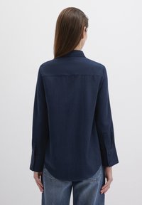 Navy blue long-sleeve shirt, smooth fabric, pointed collar, buttoned cuffs, curved hem, and a back yoke seam for added detail.