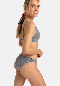 Černobílý kostkovaný bikiny set s nastavitelnými popruhy. Materiál vypadá měkký a pružný. Obsahuje design s vysokým střihem na dně.