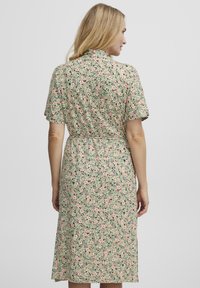 Robe fleurie à manches courtes, taille cintrée et longueur au genou, avec des motifs verts, roses et noirs sur un tissu léger.