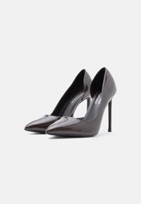 Καφέ γυαλιστερά δερμάτινα ψηλά τακούνια με μυτερή μύτη, ανοιχτές πλευρές και τακούνι στιλέτο. Λείο υλικό και κομψός σχεδιασμός.