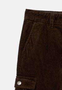 Καφέ παντελόνι από κορδούρα με κάθετες ραβδώσεις, πλαϊνές τσέπες και μανσέτα με κουμπί. Η μέση είναι ομαλή με θηλιές για ζώνη.