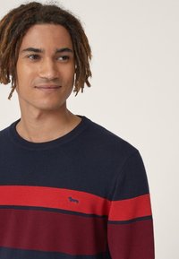 Pullover in maglia blu navy con strisce orizzontali rosse e bordeaux. Presenta un collo rotondo e un piccolo logo sul petto.