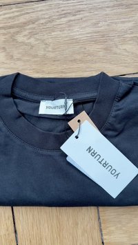 Musternöör must shirt ümmarguse kaelusega, millel on trükitud silt "YOURTURN" ja kaks kinnitatud silti heledates ja pruunides toonides.