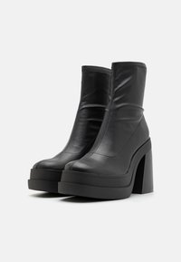 Stivali neri in pelle alla caviglia con tacco a blocco alto, finitura liscia, design slip-on e dettagli a contrasto lungo le cuciture.