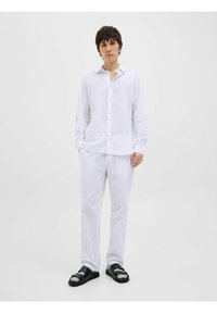 Camisa de lino blanca de manga larga con cierre de botones, combinada con pantalones a juego y sandalias negras con diseño de doble correa.