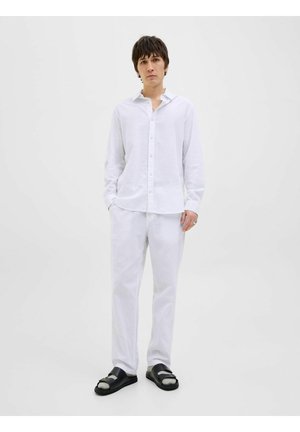 Witte linnen overhemd met lange mouwen en knoopsluiting, gecombineerd met bijpassende broek en zwarte sandalen met een dubbelbandontwerp.