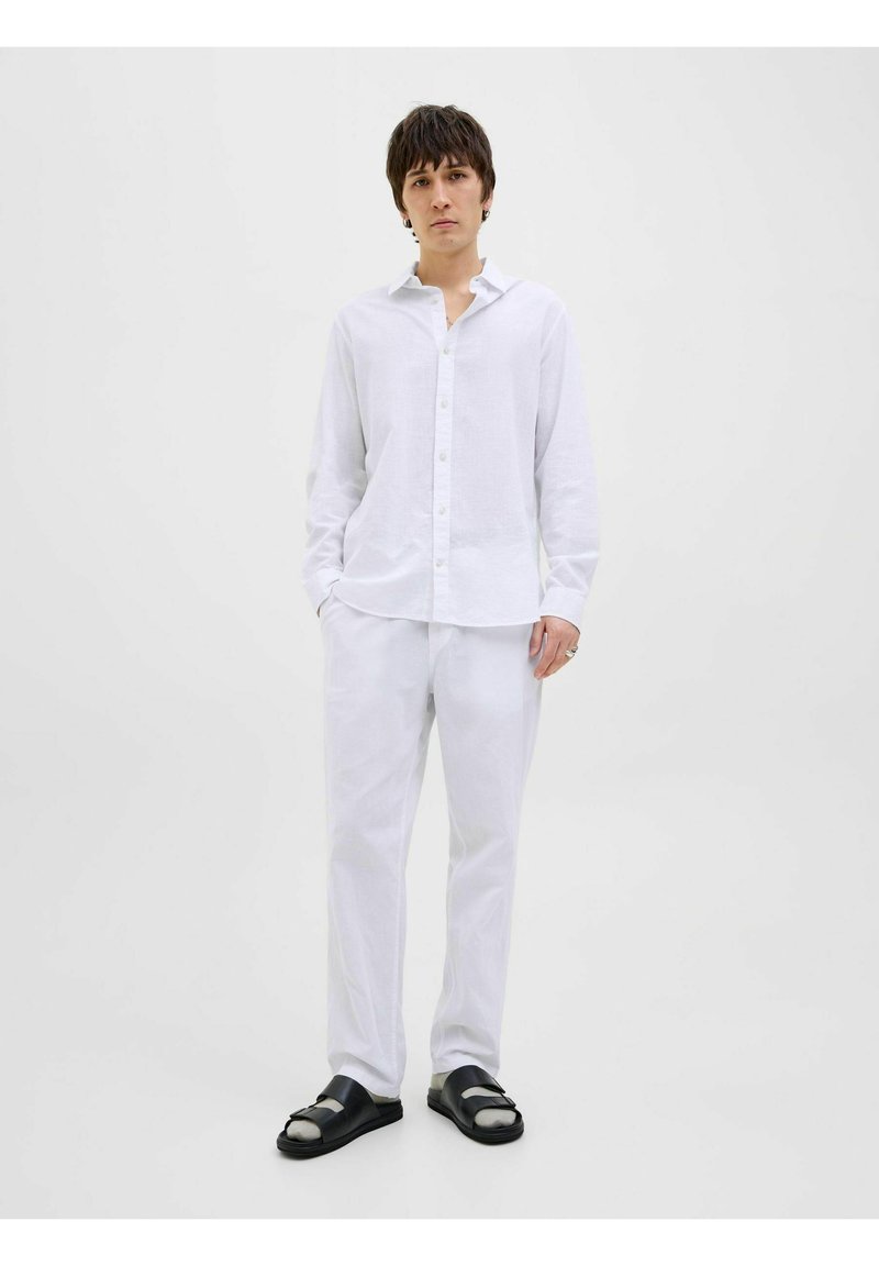 Camisa de lino blanca de manga larga con cierre de botones, combinada con pantalones a juego y sandalias negras con diseño de doble correa.