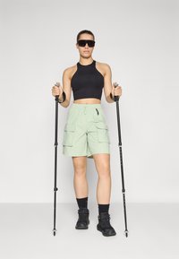 Musthave musta ilma varrukat crop top, hele roheline cargo lühikesed püksid taskutega, mustad matkasaapad ja matkakepid. Sile kangas, sportlik lõige.