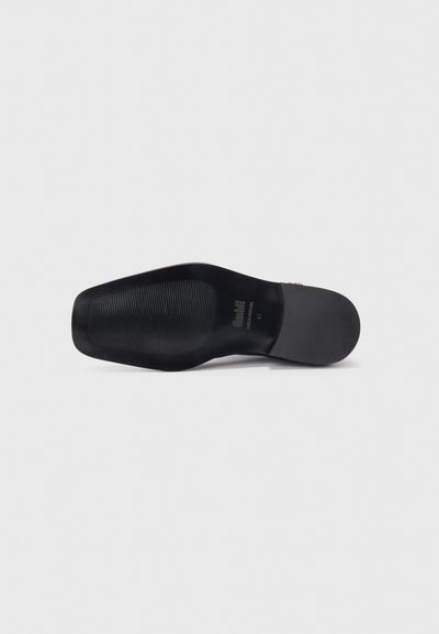 Suela de zapato negra con goma negra texturizada. Presenta un nombre de marca en relieve y un indicador de tamaño. Bordes suaves y una ligera curva en la puntera.