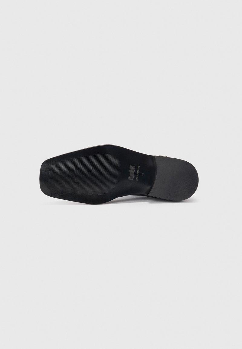 Semelle de chaussure noire en caoutchouc texturé. Présente un logo de marque en relief et un indicateur de taille. Bords lisses et légère courbure au niveau des orteils.