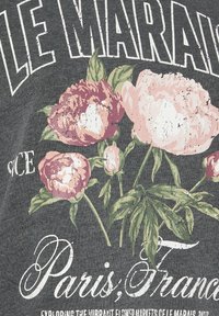 Tela gris oscuro con un diseño floral que presenta peonías rosas y hojas verdes. Texto en blanco que dice "LE MARAIS" y "París, Francia".