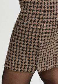 Rjava in črna obleka s houndstooth vzorcem, ki ima prilegajočo zasnovo, teksturirano tkanino in majhno režo na robu.